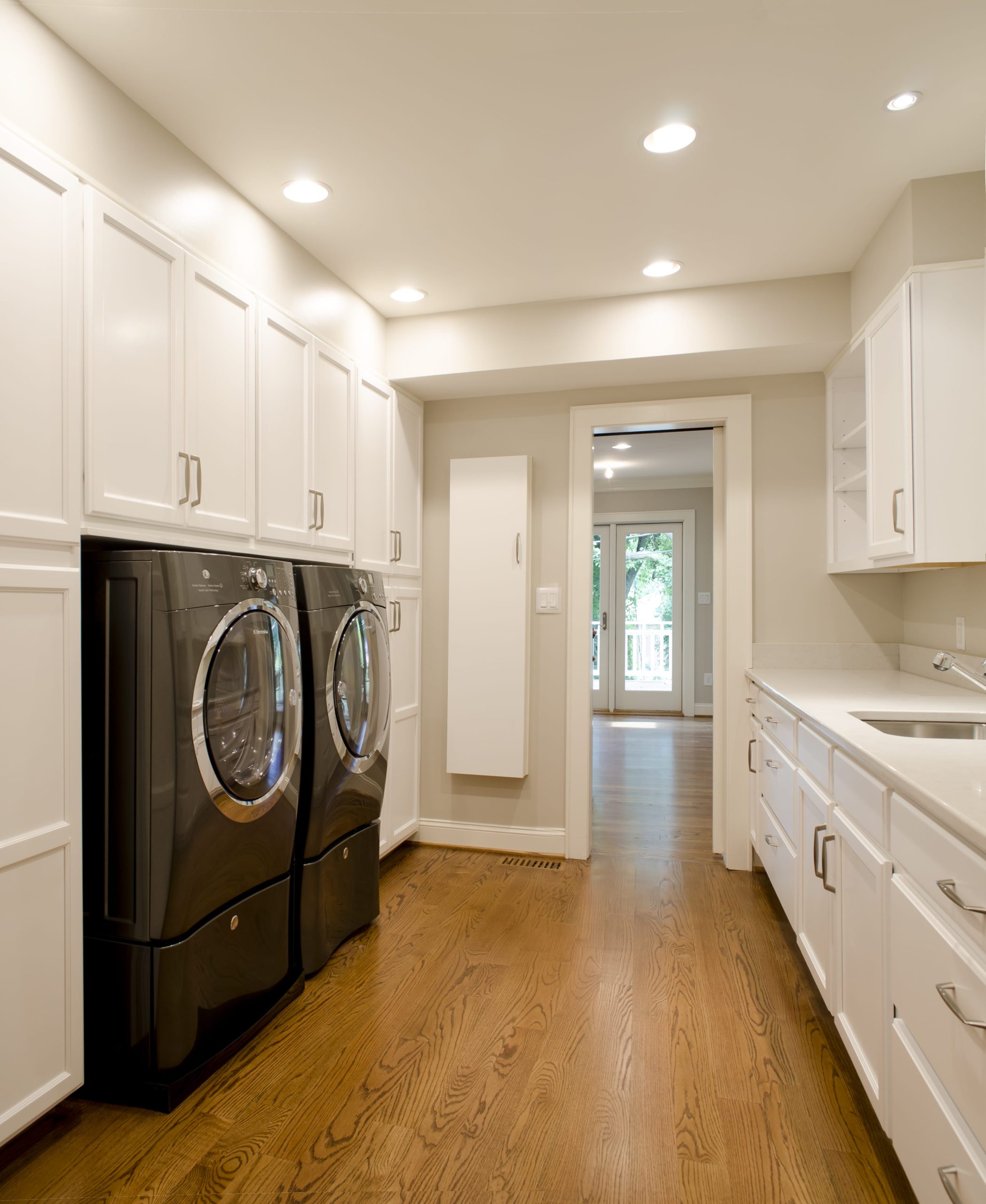 A clean and efficient laundry room with large built-in cabinets, shelves, counter space and deep sink