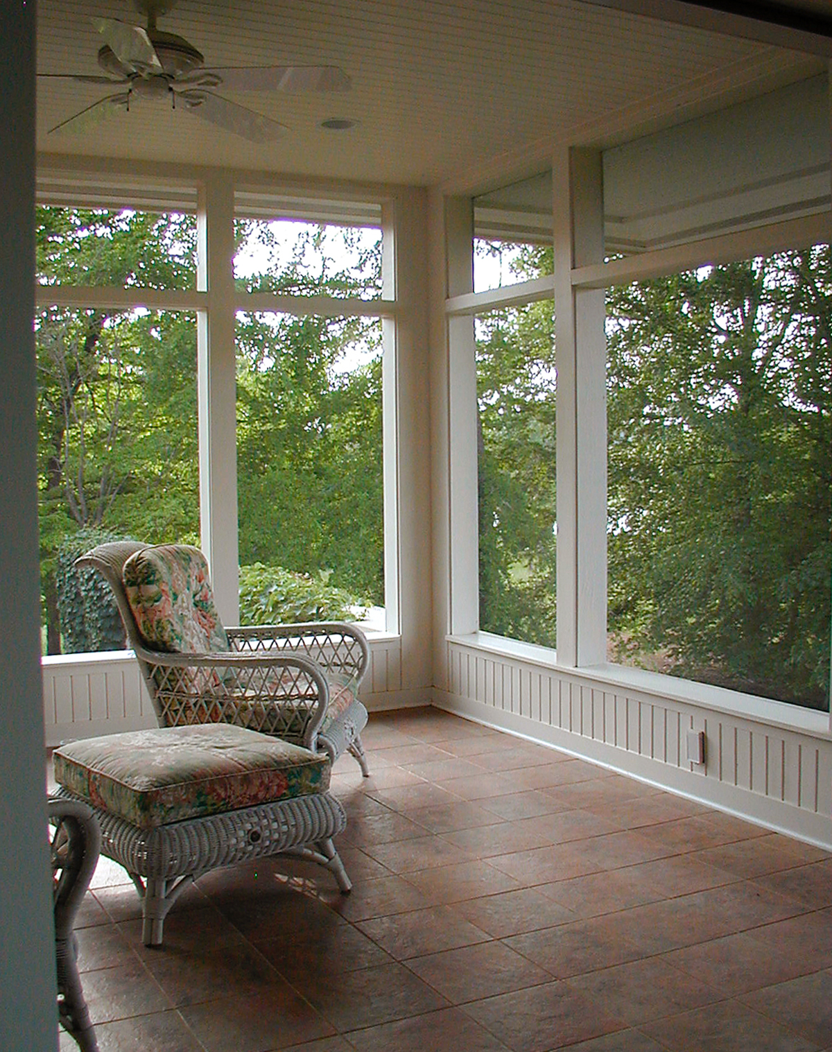 A simple and elegant screened porch with tile floors and a cozy armchair overlooking the wooded surroundings.