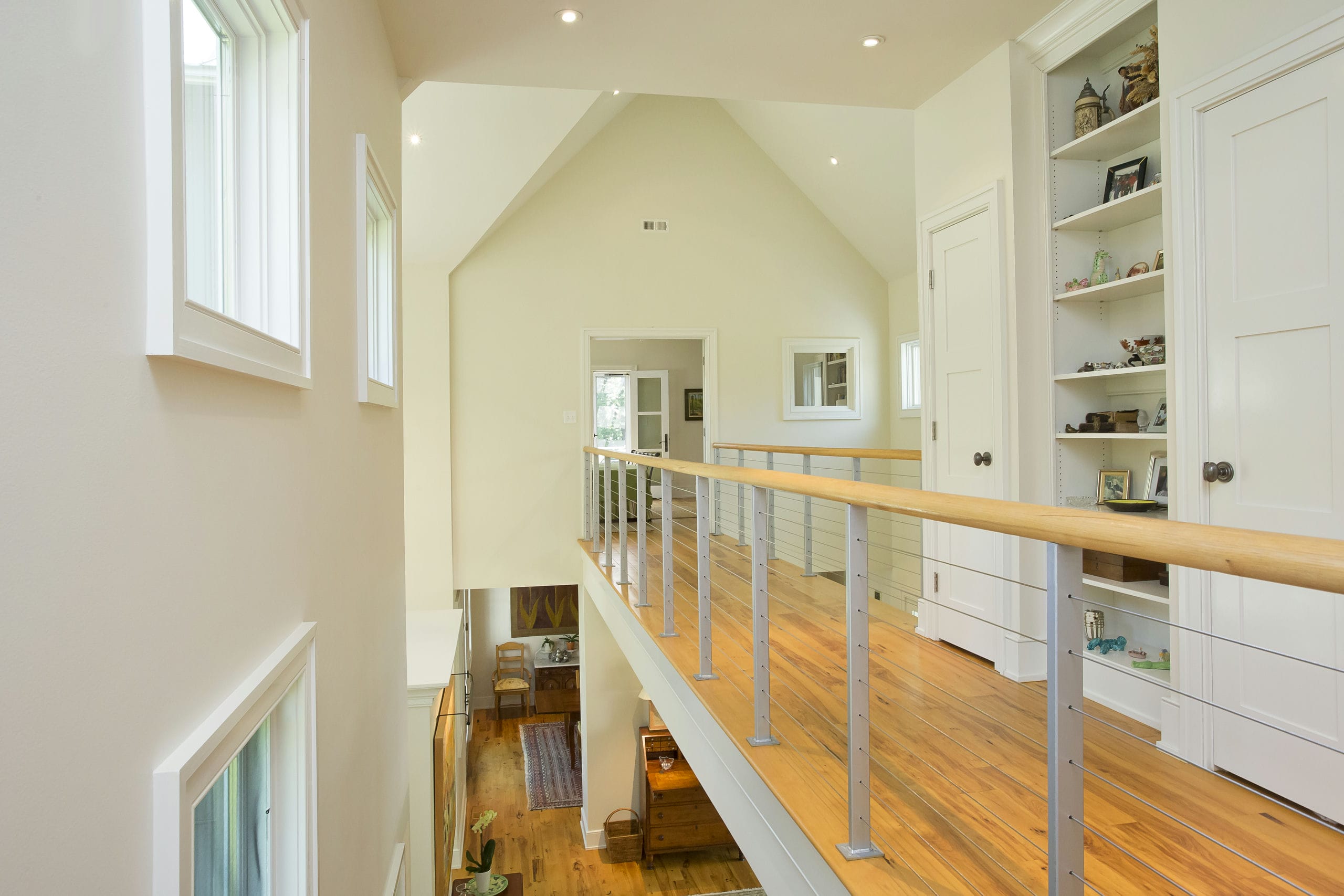 Catwalk with modern cable railing passing through double height foyer with vaulted ceilings