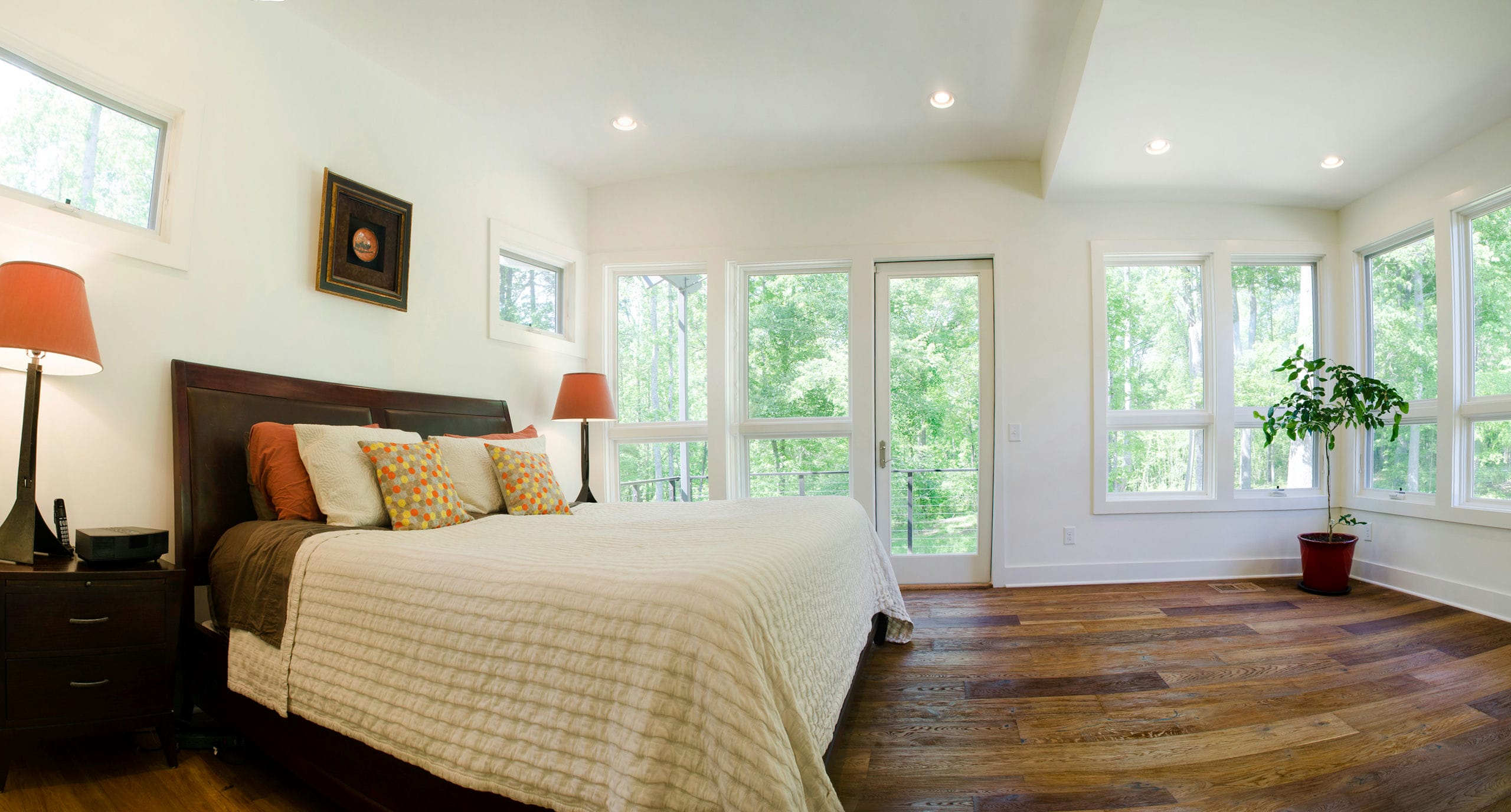 Bright and airy primary bedroom with rustic wood floors and and corner windows and balcony