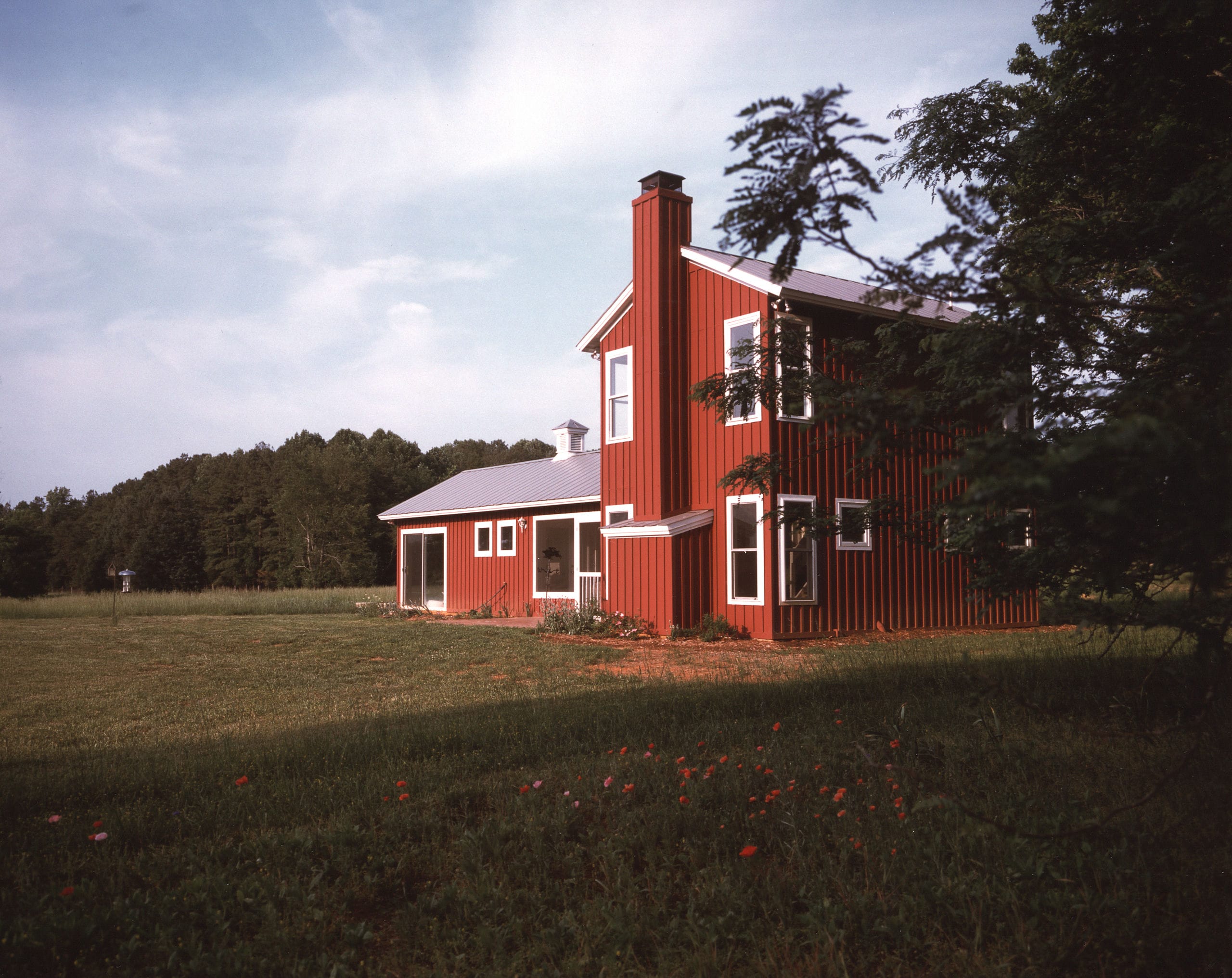 Two story tiny-house with red board and batten siding in a meadow