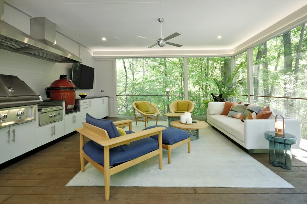 A bright and contemporary screened porch with fully outfitted outdoor kitchen overlooks a lush, green forest.