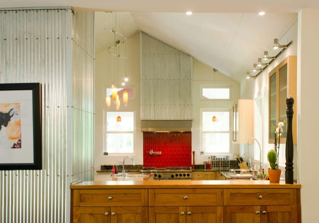 Bright and open contemporary kitchen with tall cathedral ceilings, wood cabinetry and artistically placed corrugated metal and red tiles along the back wall.