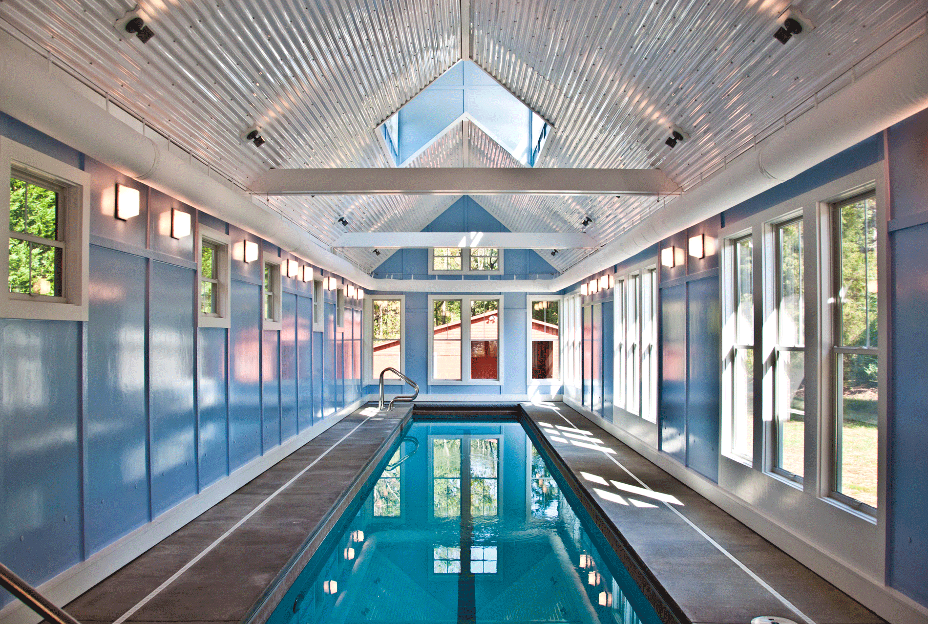 A bottom lit indoor lap pool in a bright and airy room with vaulted corrugated metal ceiling