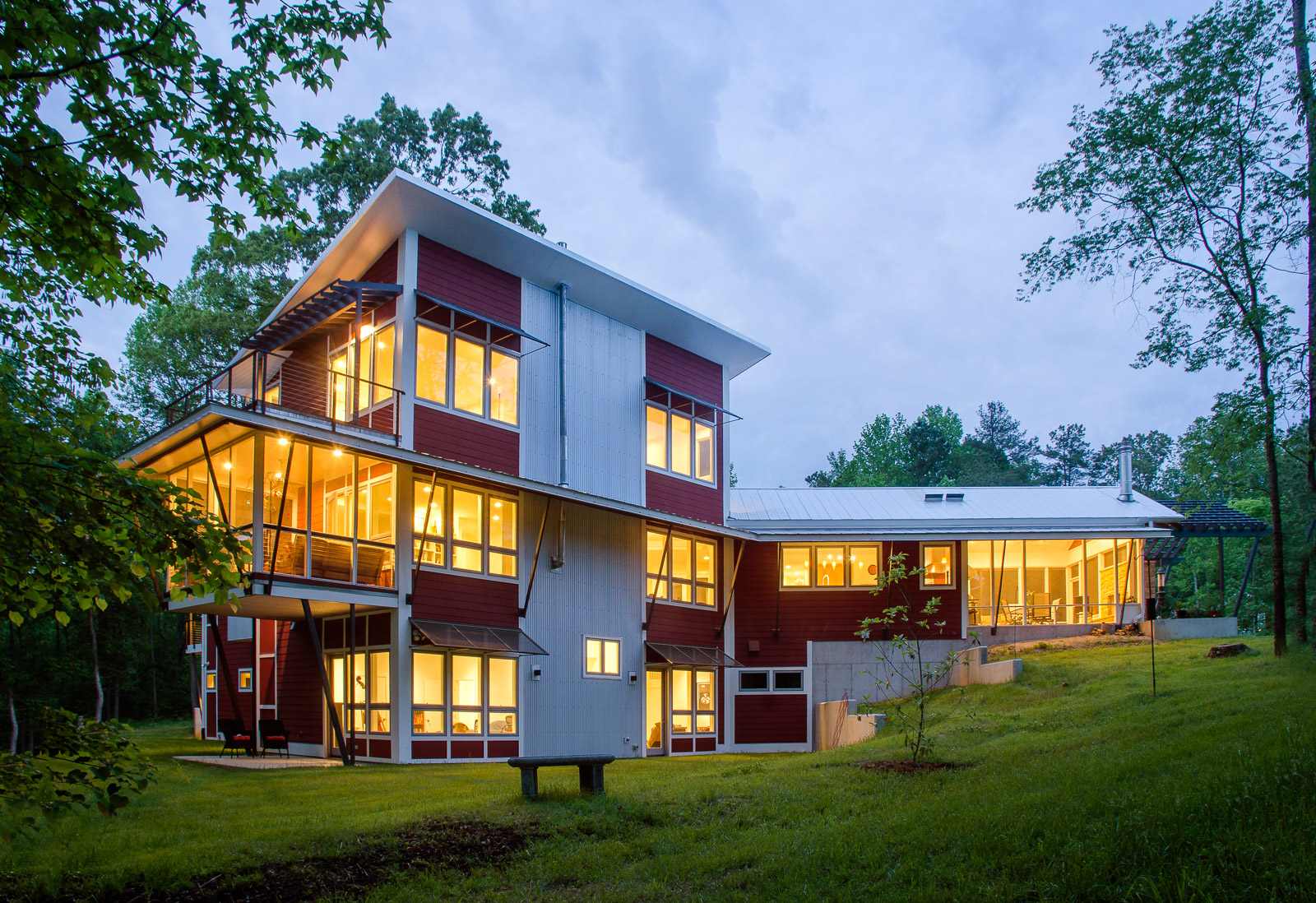 Contemporary house with distinct one story and three story volumes. Large windows wrap the house creating unique elevations with shading elements, a cantilevered porch and metal siding and roof.
