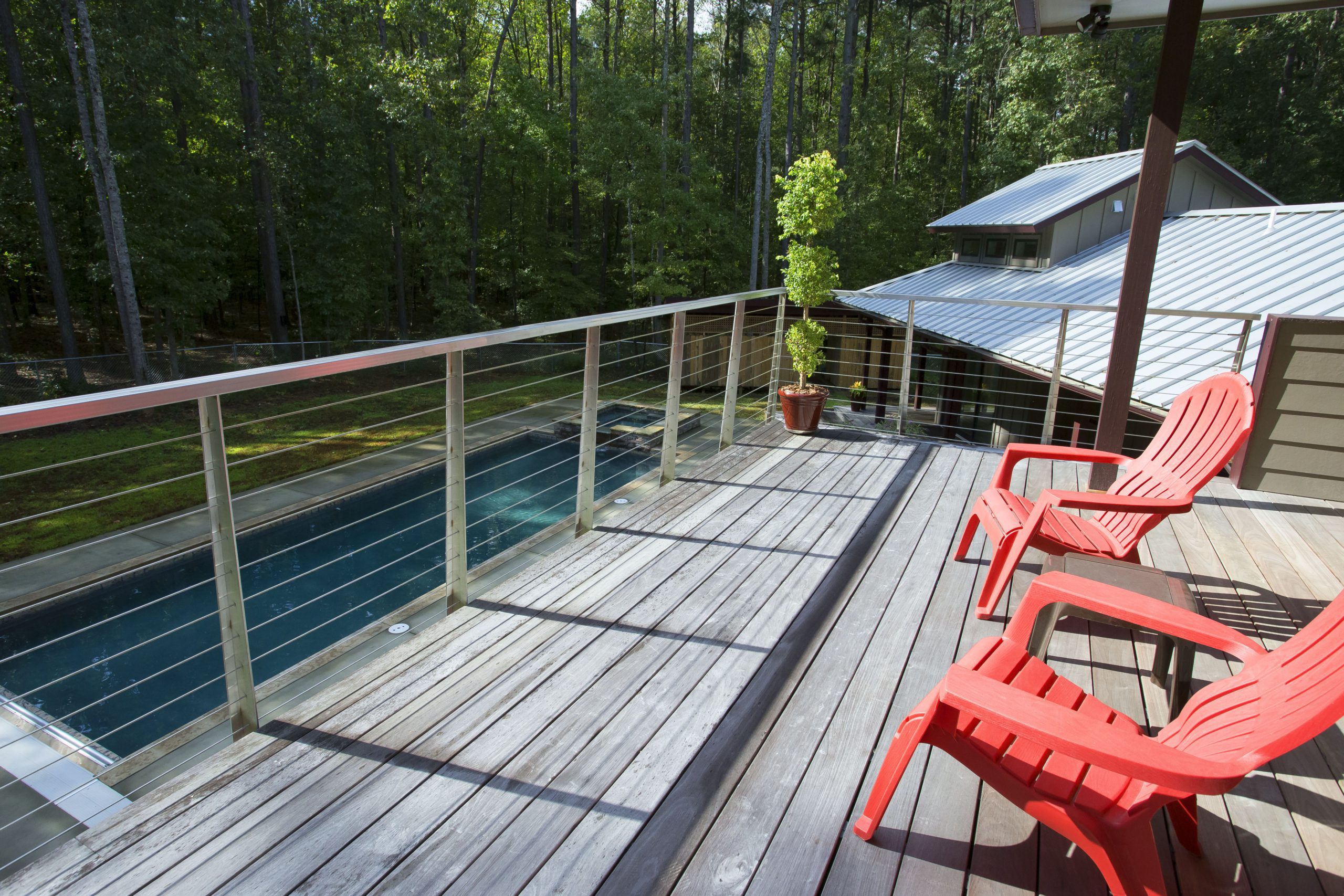 Large upper level terrace with cable railing overlooking pool nestled in the forest