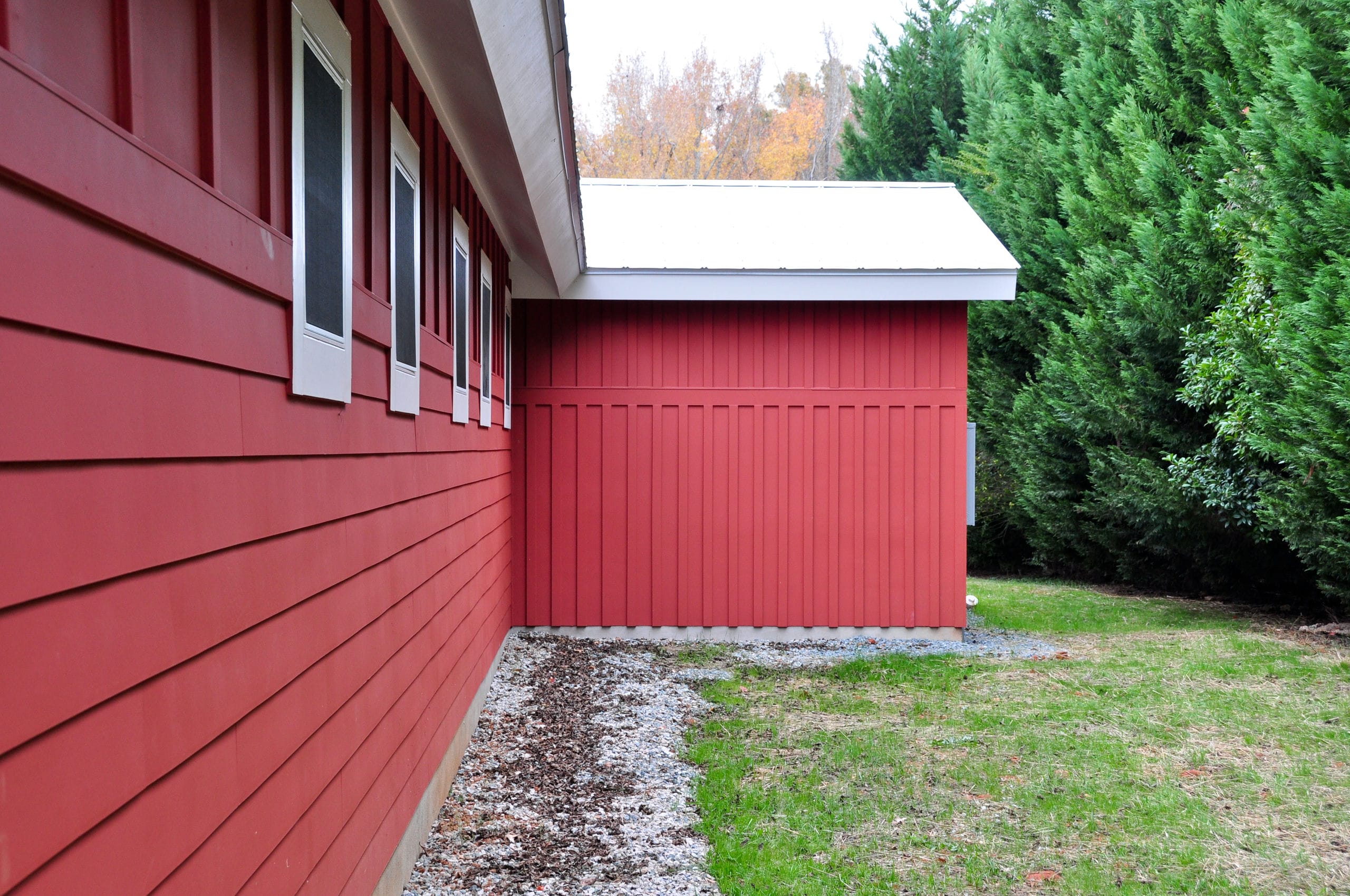 Red board and batten siding on a small pool house set against verdant trees