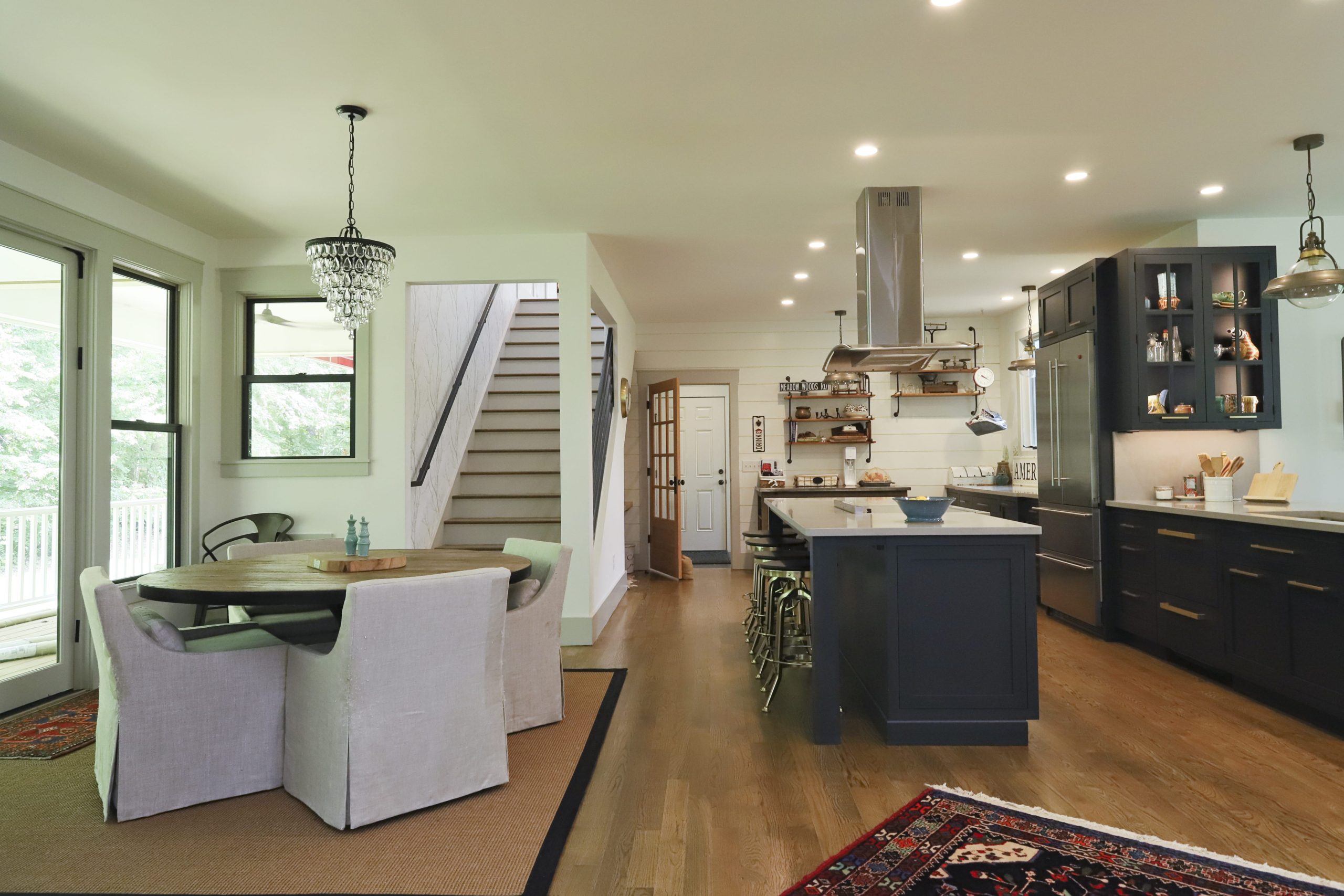 An open-plan kitchen, adjacent to a covered porch, has a large central island, dining nook, and floating shelves.