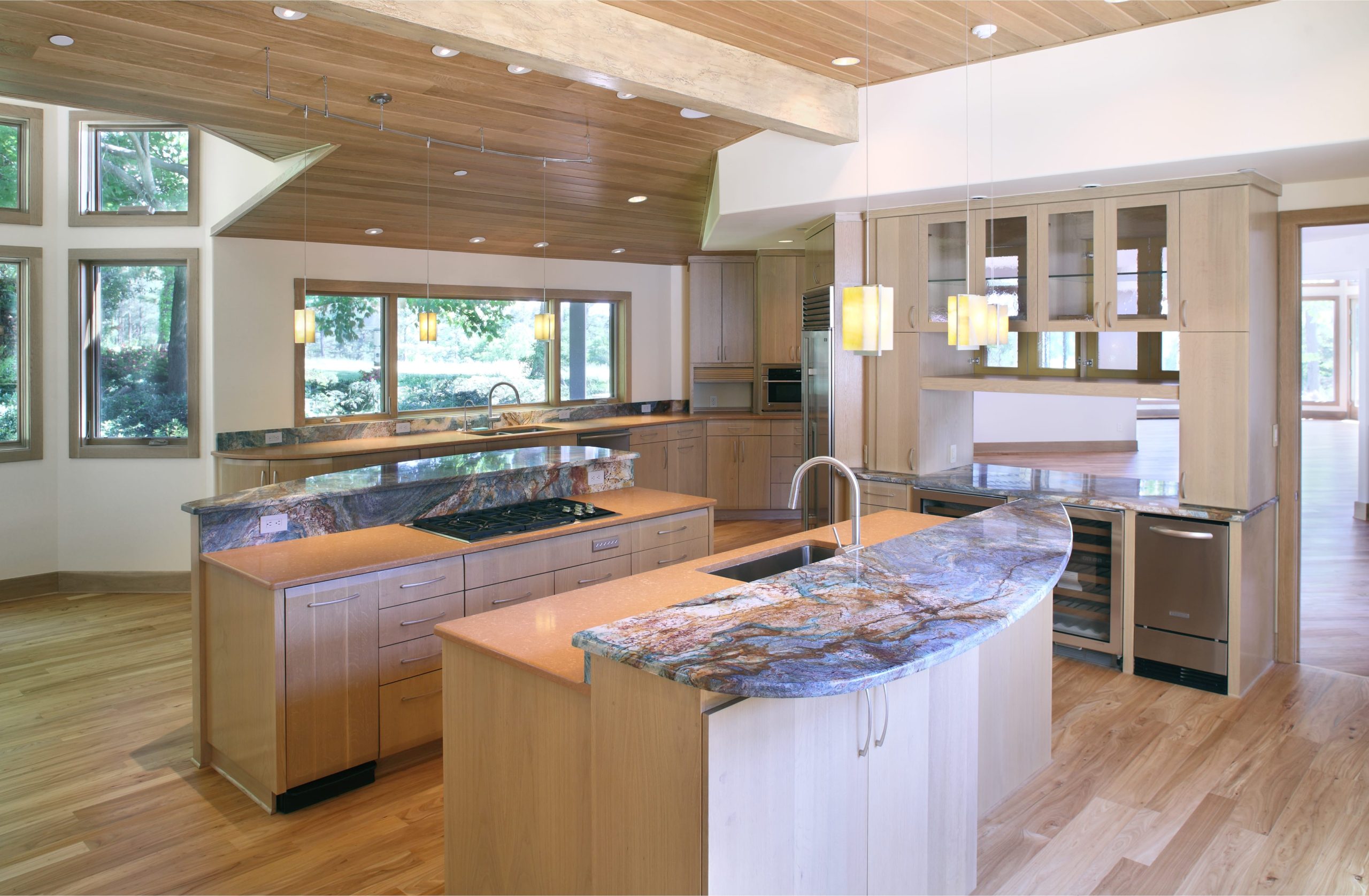 A bright and open kitchen with natural wood cabinets, stone countertops, bar seating and high ceilings occupies unique and angular spaces within the house.