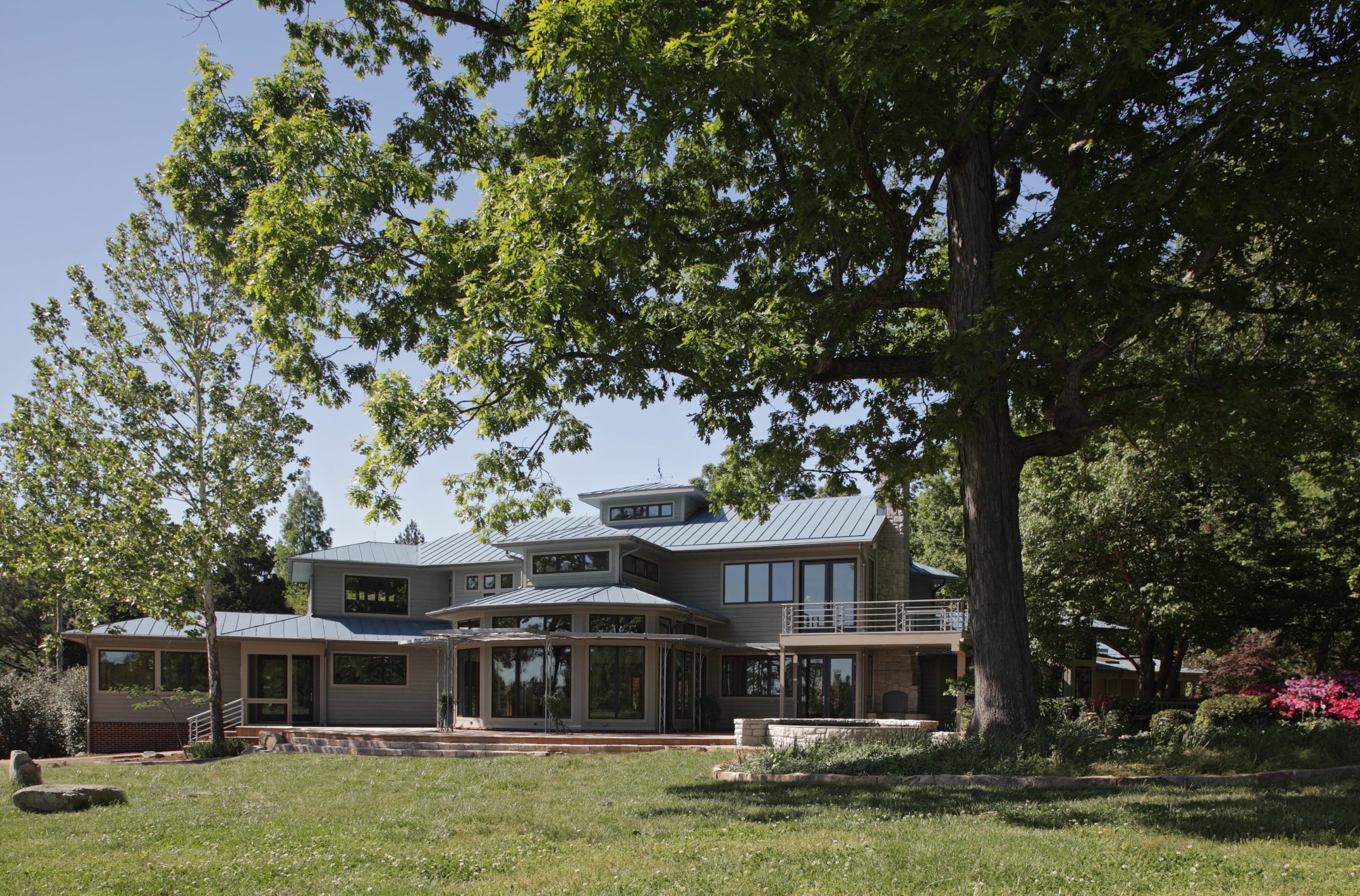 Lush gardens and large oak trees surround the house. A variety of covered and uncovered outdoor spaces and large expanses of glass connect the house to its spectacular site.
