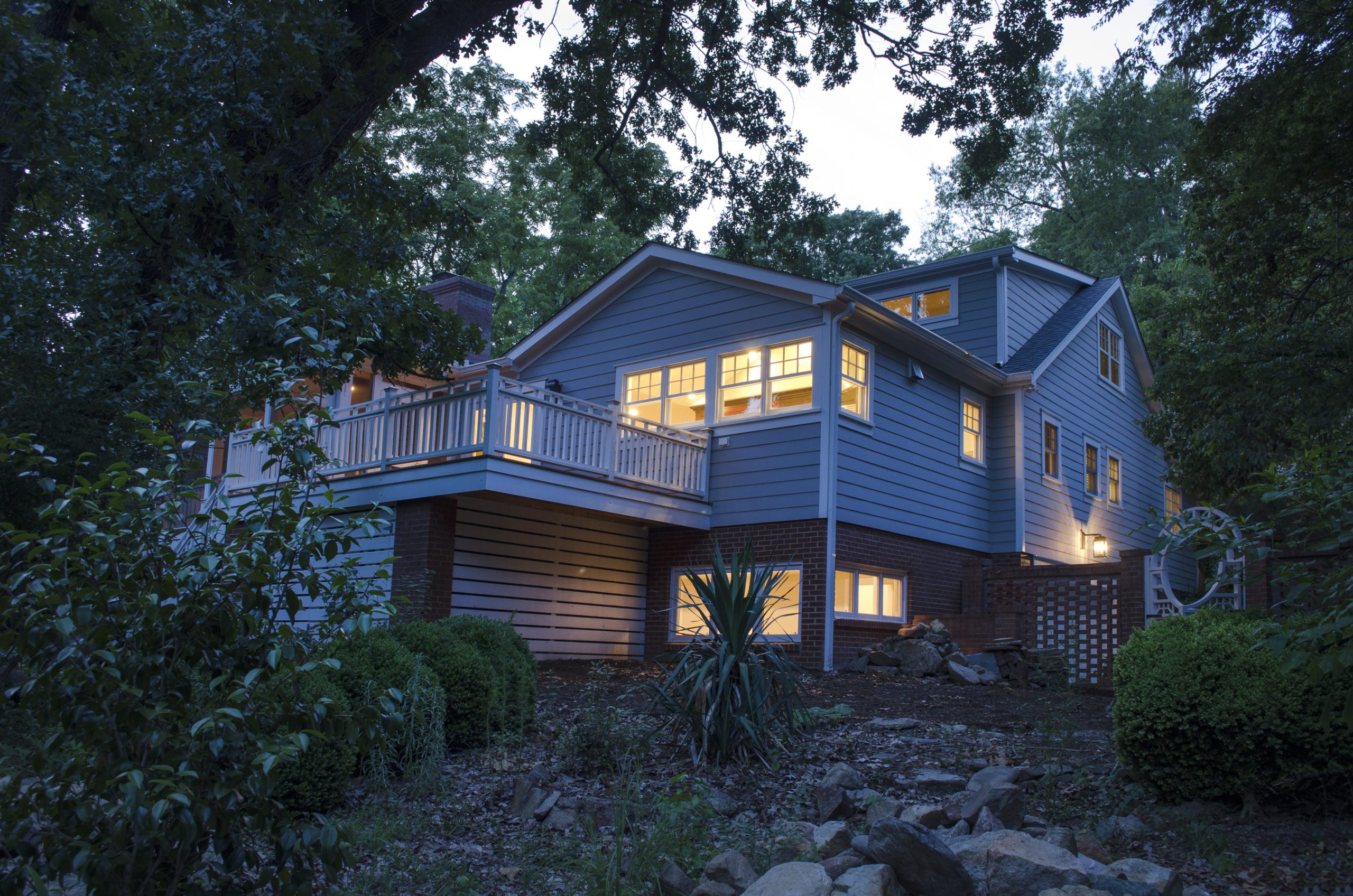 An exterior view of the back of the house at dusk, showing the new deck and porch as the house emits a warm glow from within
