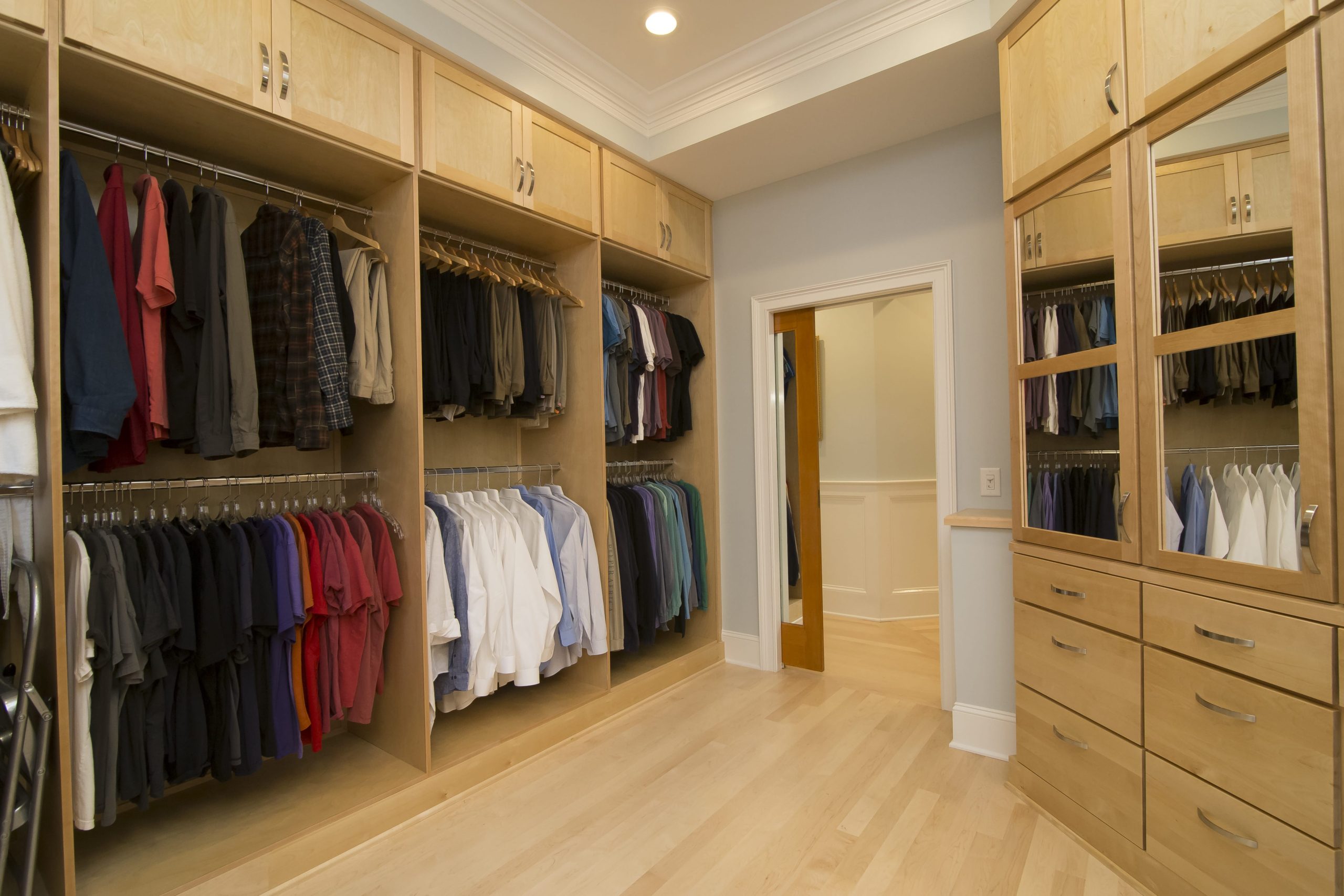 The cabinetry and floor of the primary closet are a matching light colored wood, creating a peaceful, monochromatic palette in the space.