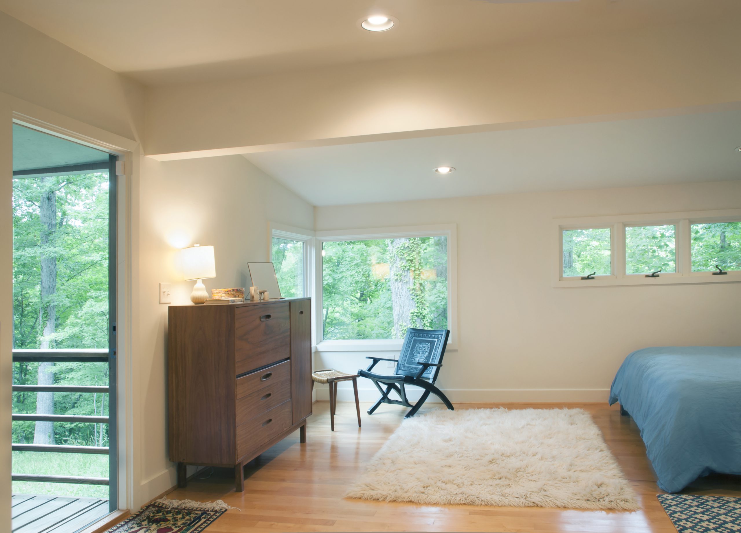 A simple yet sophisticated bedroom with a cozy seating area with corner windows and a door connecting the space to a porch