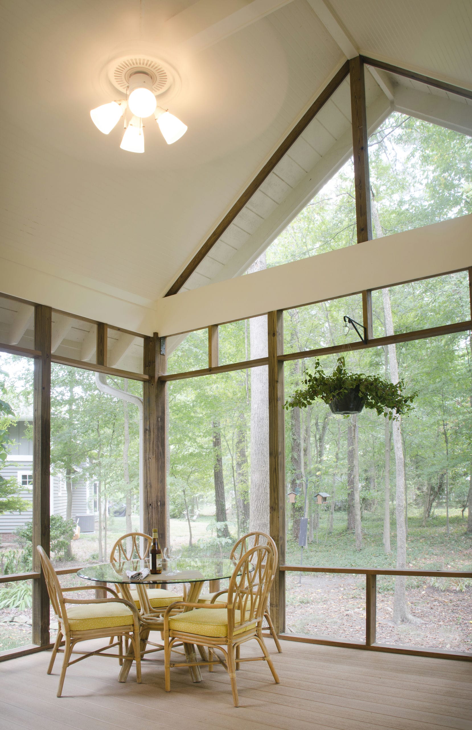 Interior of vaulted screen porch with white beadboard ceilings and dark wood posts nestled in forest