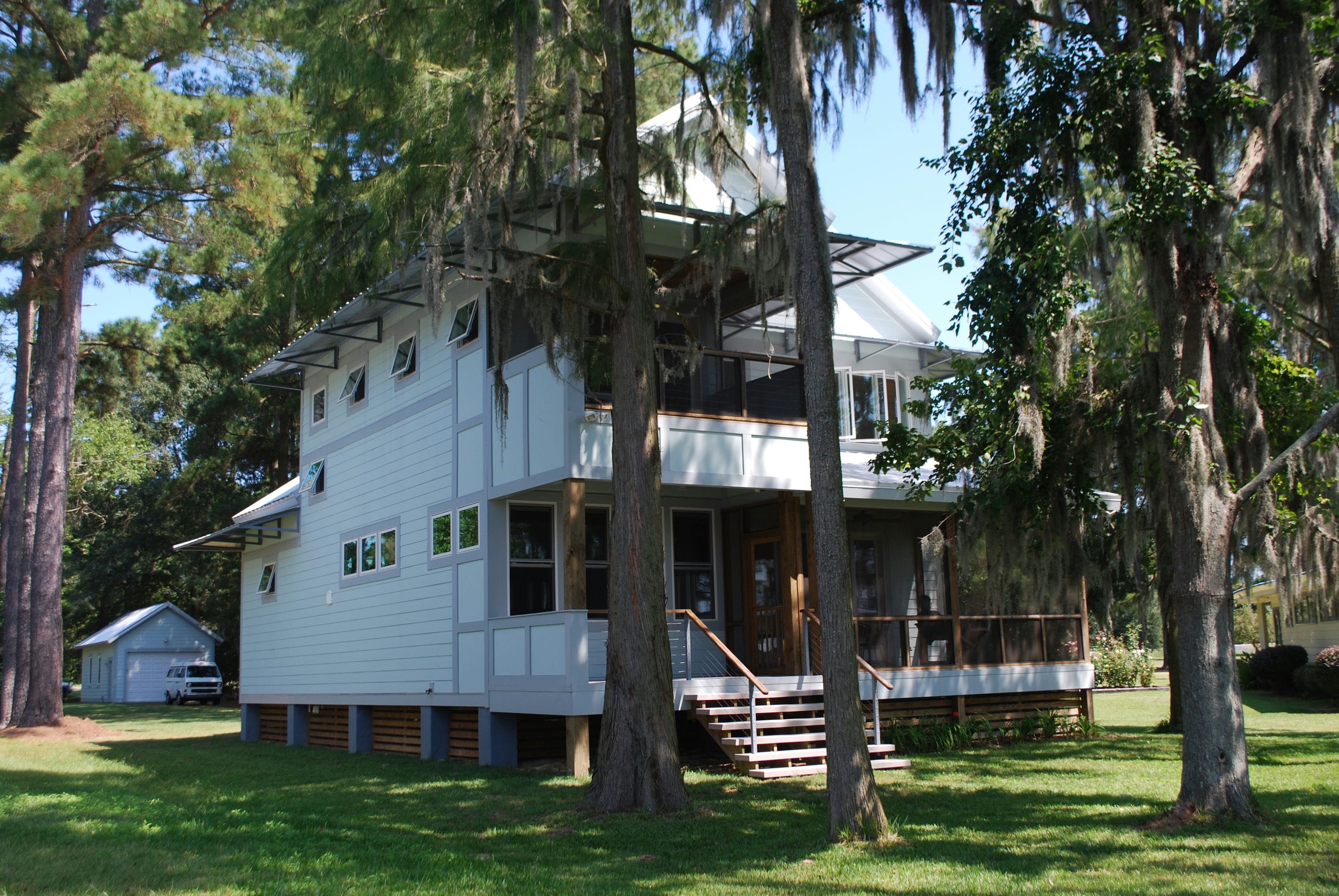 Modern coastal home with many porches shaded by trees covered in Spanish moss.