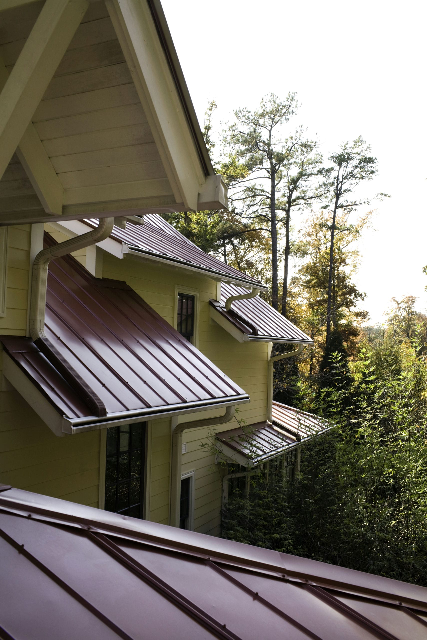 A detail view of red standing-seam metal roof forms appearing to cascade down the wooded landscape
