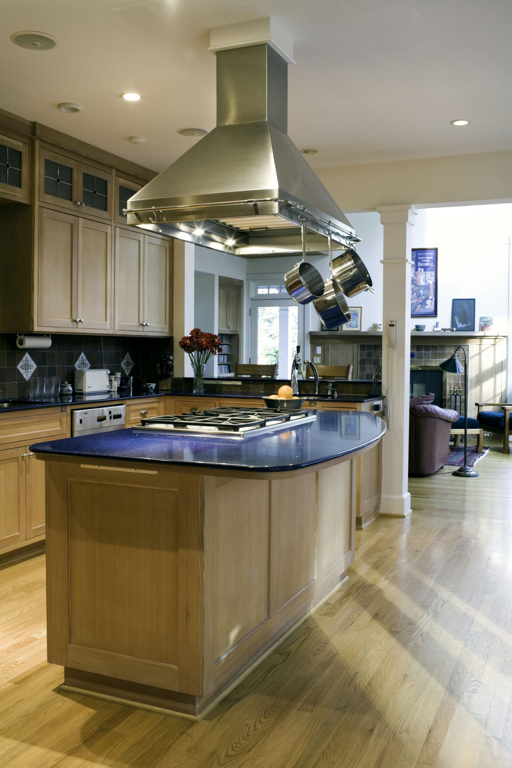 A kitchen with generous cooking island, metal range hood and natural wood cabinets opens up to the living space