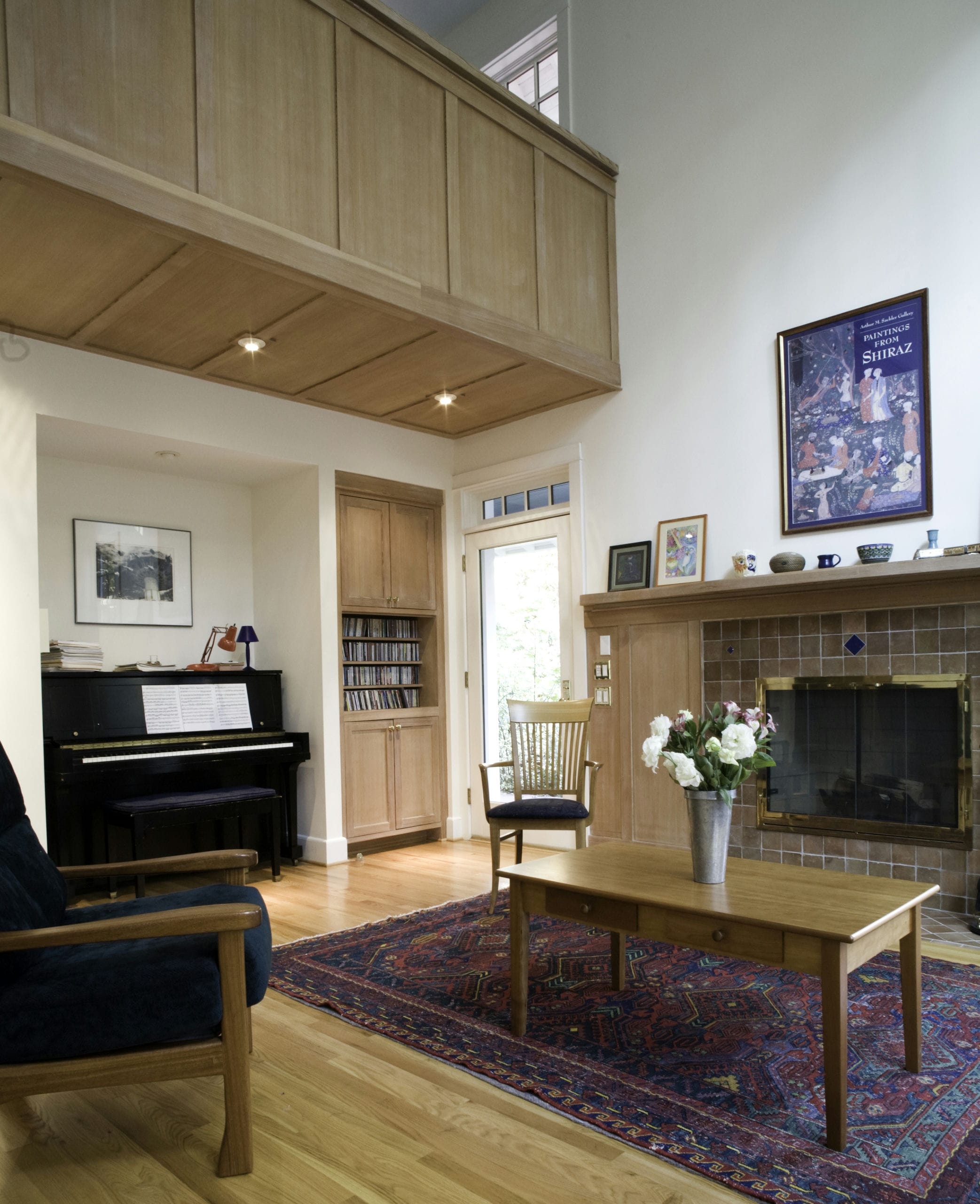Double height living space with upstairs mezzanine, built-in coves for a piano and bookshelves, and a central fireplace.