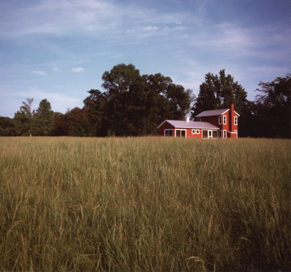 Red gabled house nestled in a grassy meadow set against a tree line