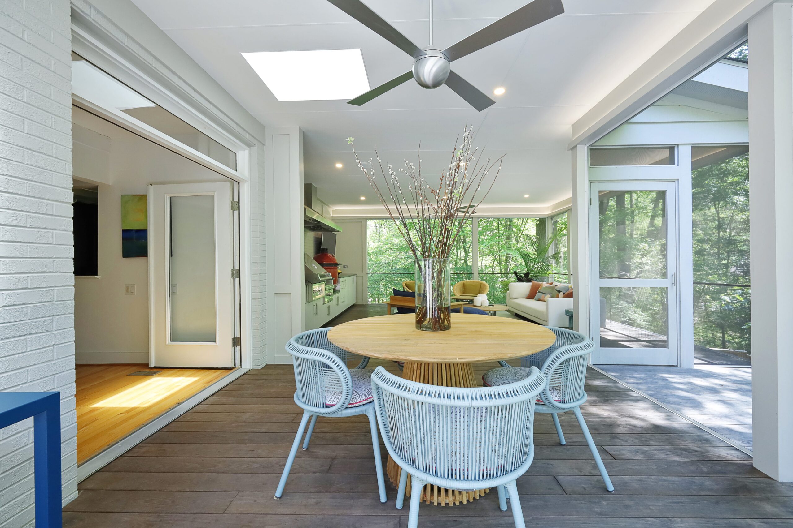 A contemporary dining table, located just outside the large French doors connecting to the main house, sits under large skylights in the screened porch.