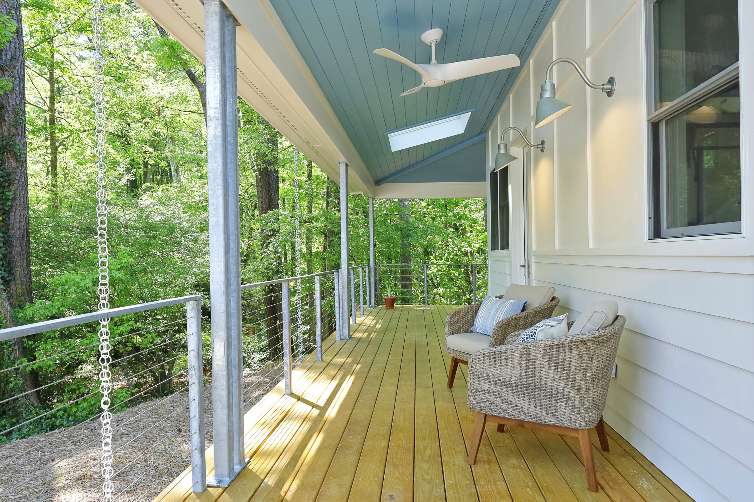 An exterior view of a covered porch with skylights, painted blue ceiling, galvanized steel railings and columns, and board-and-batten white siding