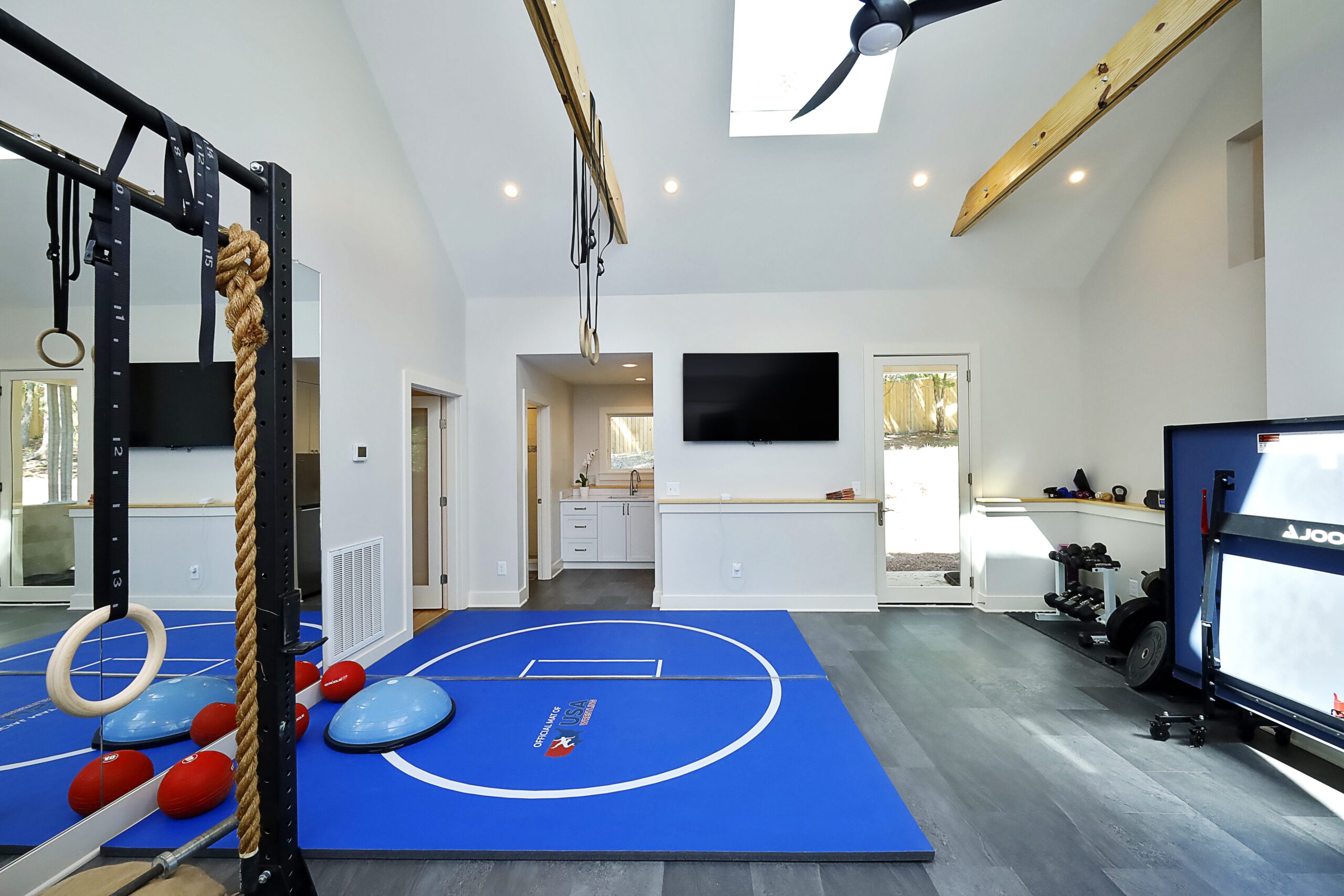 A view of the home gym looking towards the kitchenette. Skylights in the high ceiling bring ample light into the space.