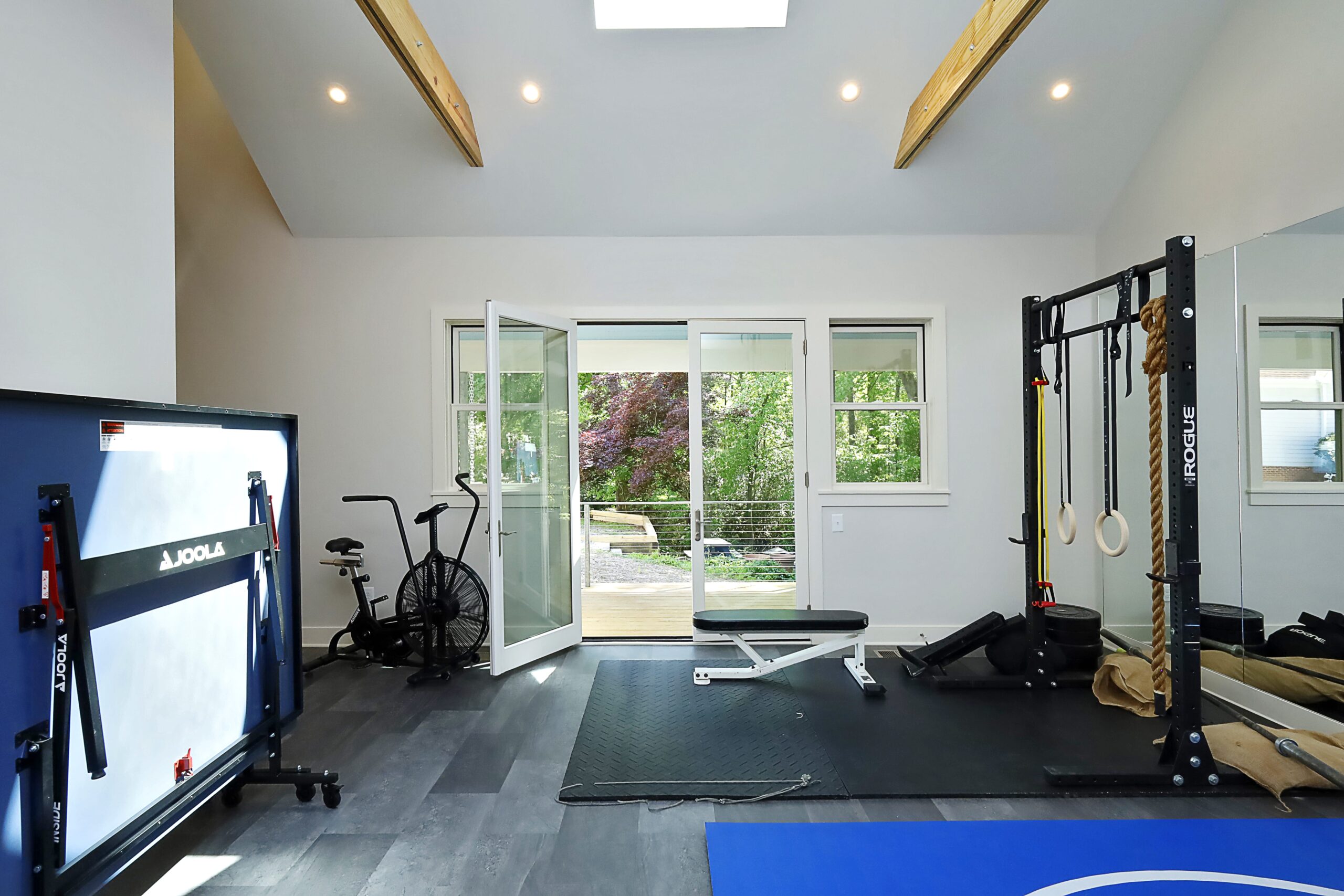 A view of the home gym looking out towards the covered porch. Tall glass double-doors connect the two spaces.