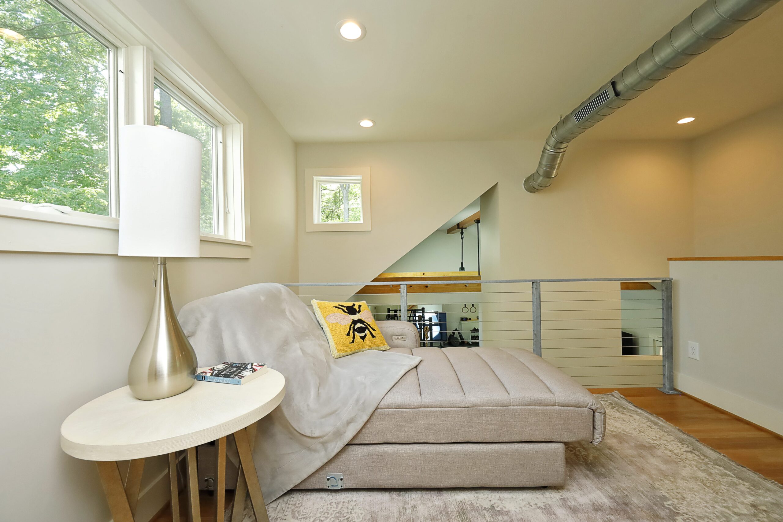 A chaise lounge sits in the new loft, overlooking the elegant stair and home gym. The loft is surrounded by windows and unique interior cut-outs that open up the space.