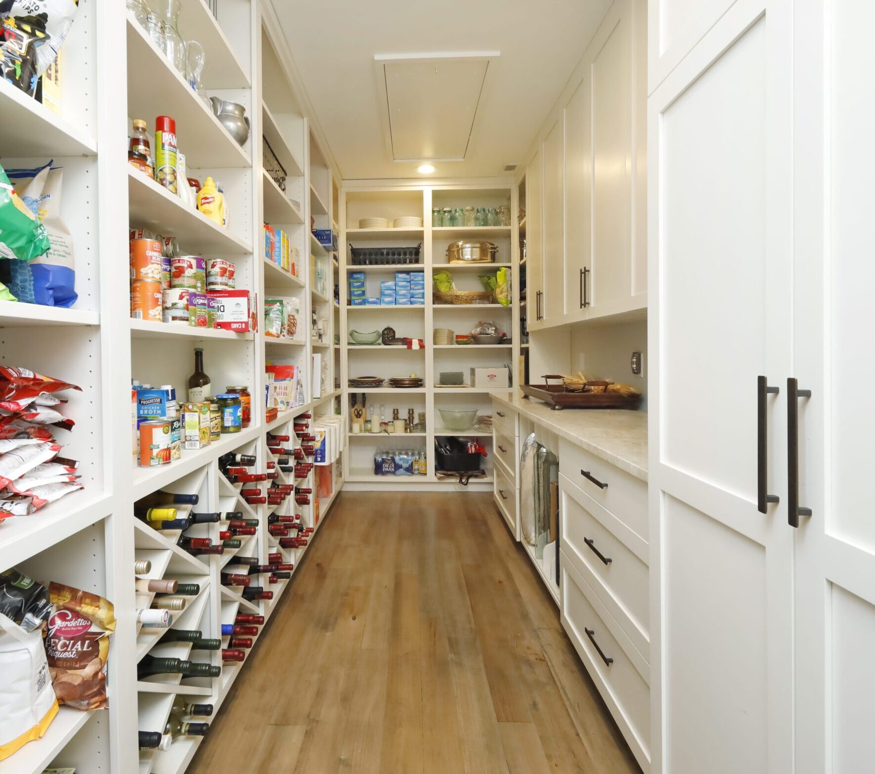 A generous pantry with clean, white built-in storage, wine racks, cabinetry and counter space.