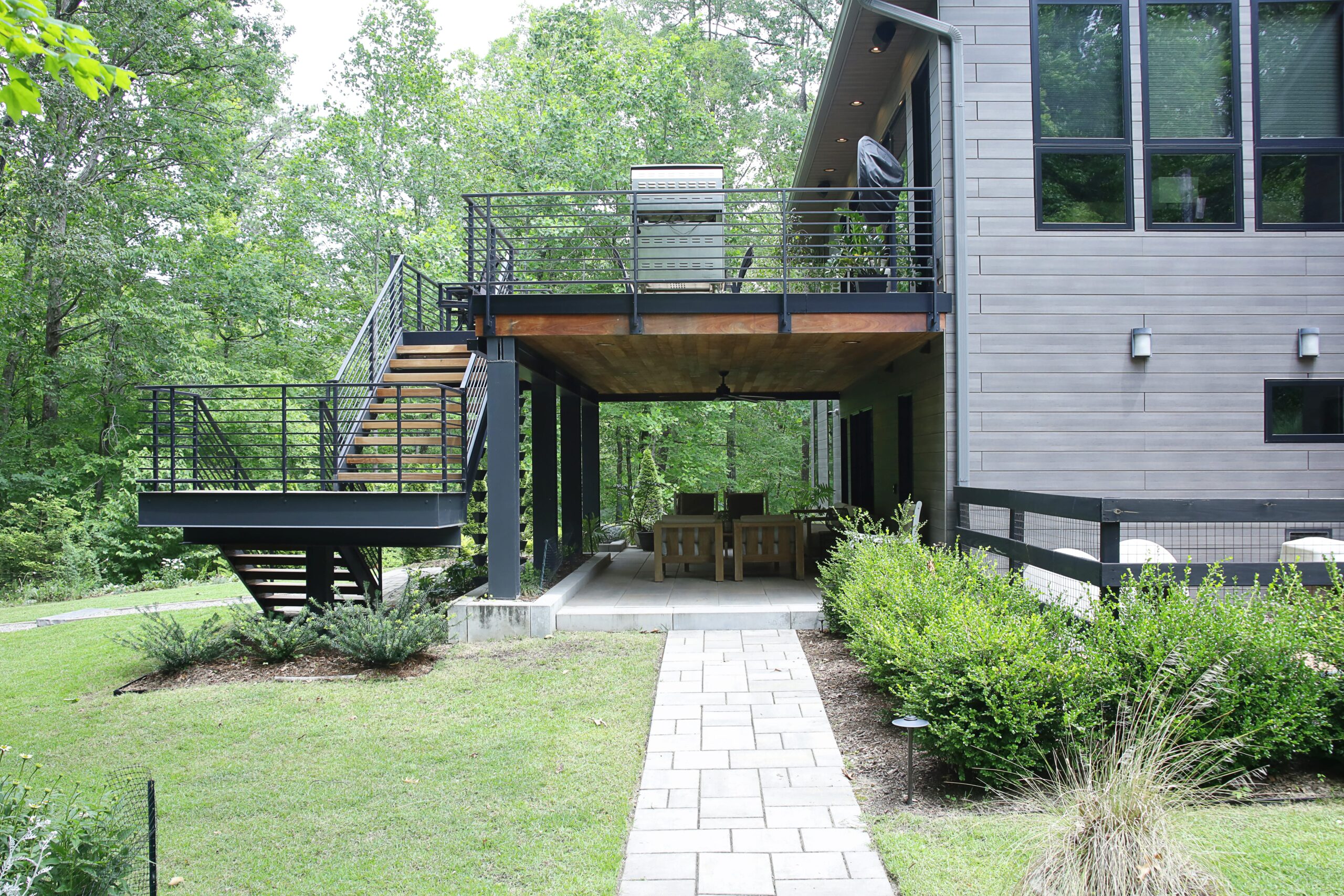 A lower level patio is shaded by an upper level balcony, connected by an open-riser steel staircase.