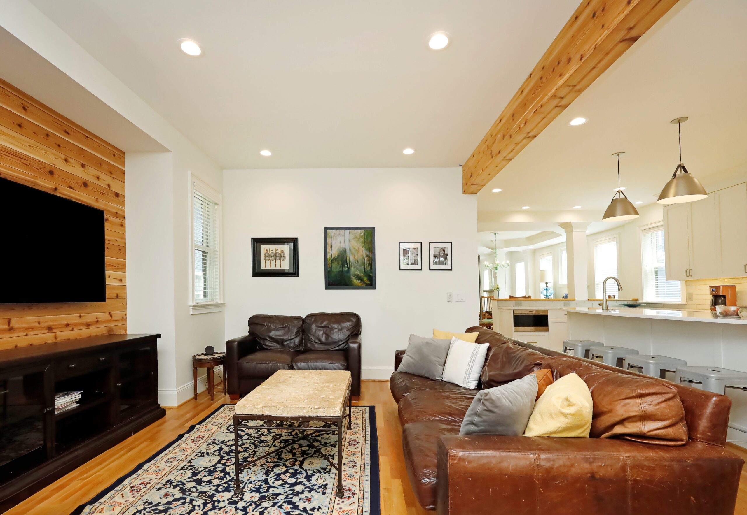 The living room, directly adjacent to the kitchen, benefits in spaciousness from the open-concept plan. It feels visually distinct because of a wooden dropped beam and cozy heart-pine wall finish along the entertainment center niche.