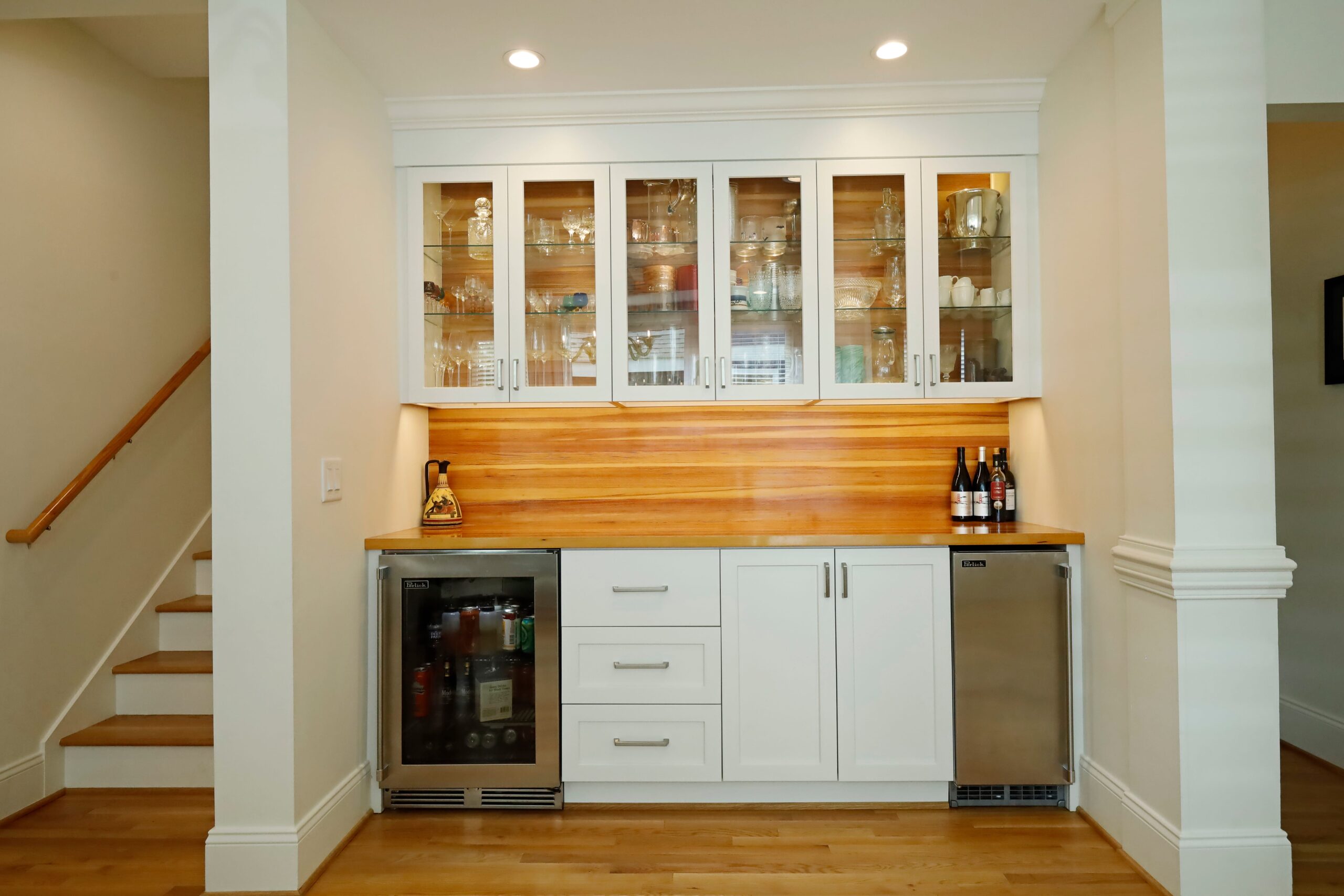 A built-in bar with glass-front cabinetry, under-counter fridge and ice-maker, and custom heart-pine countertops and wall finish.
