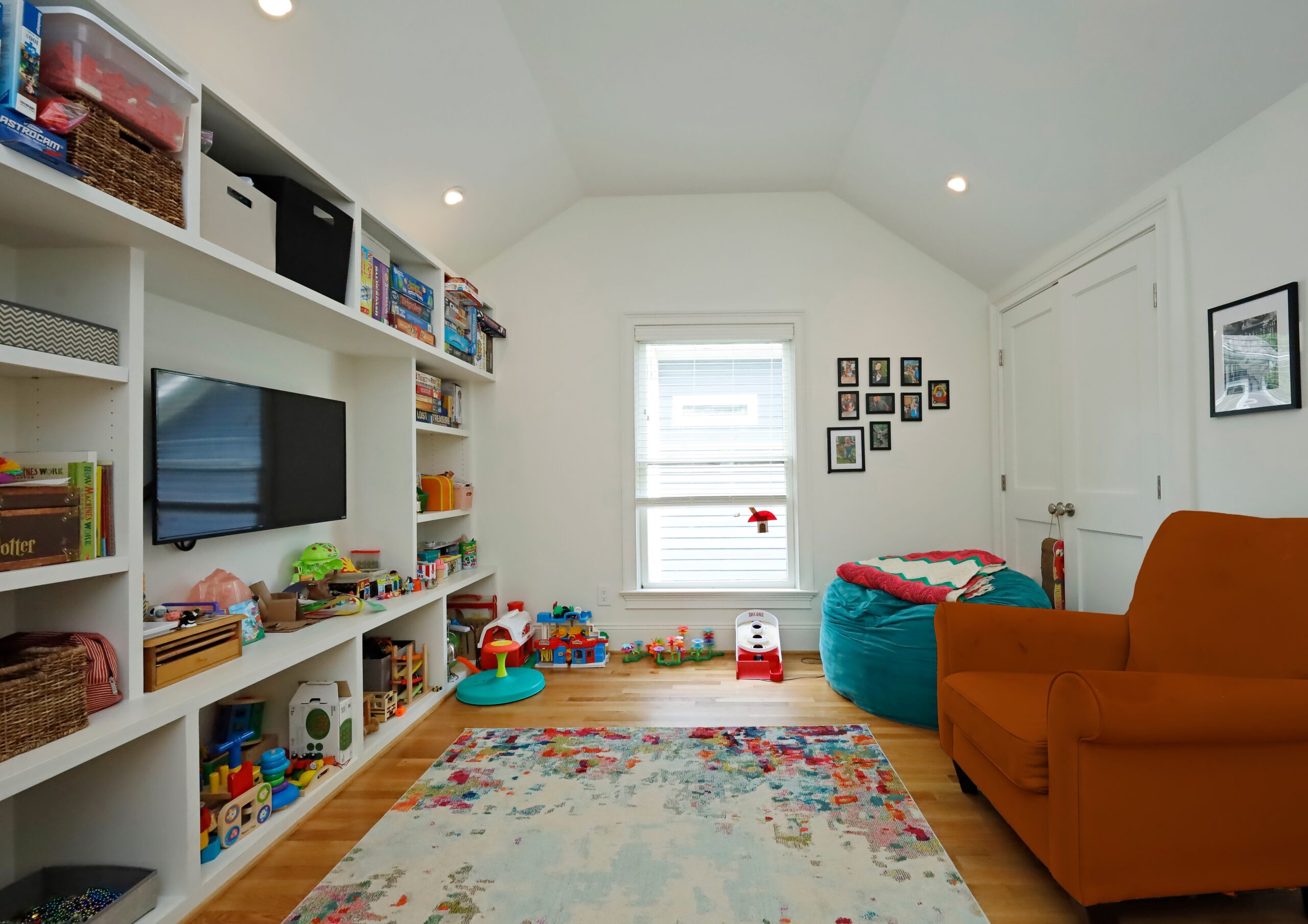 A bright and open playroom space with a wall of built-in storage for games, toys and and entertainment center.