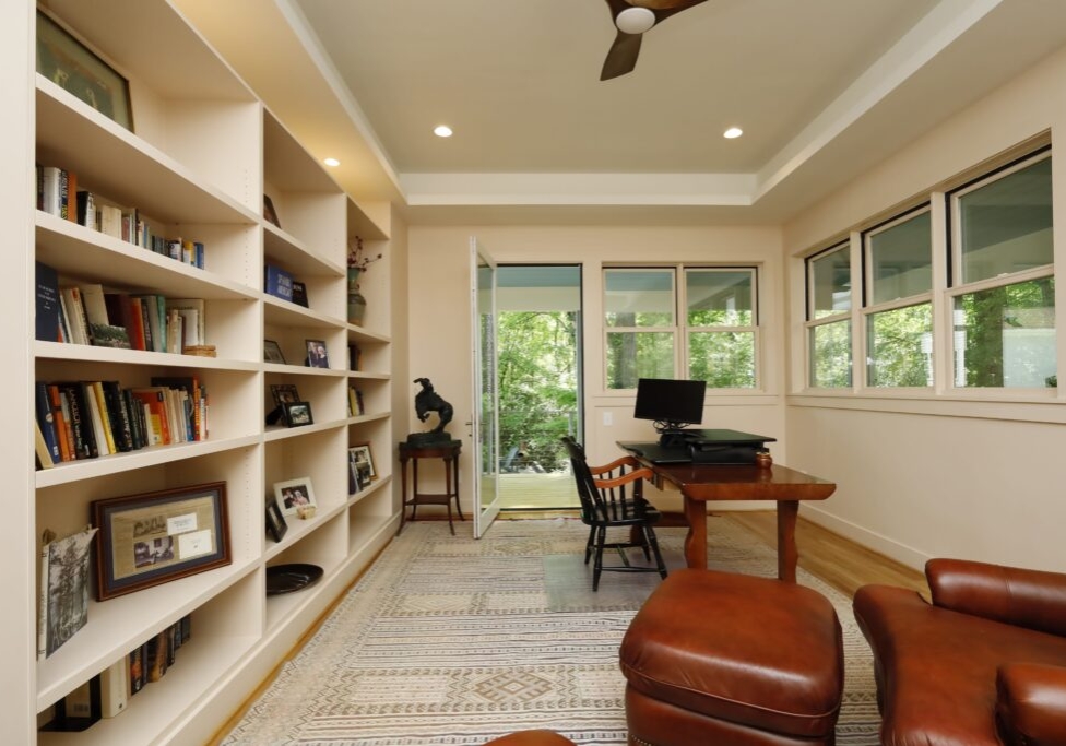 A peaceful home-office space with generous windows, tray ceiling and large built-in bookshelves lining the back wall.