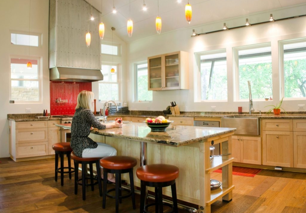 Large windows, tall ceilings, corrugated-metal-wrapped range hood, and generous kitchen island with metal accents create a dynamic and functional kitchen.